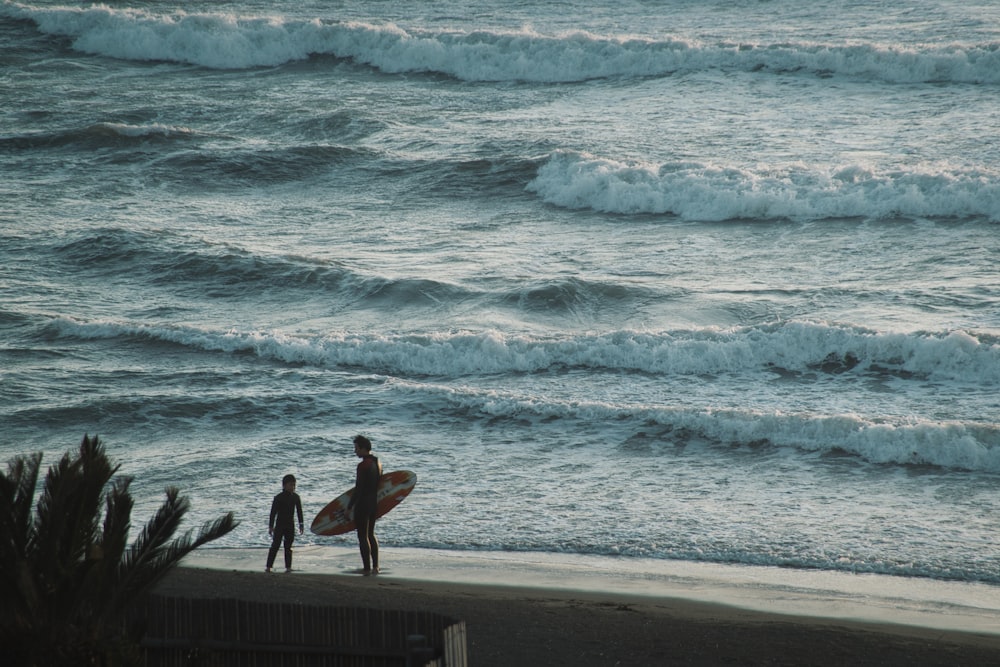 a couple of people standing on top of a beach next to the ocean