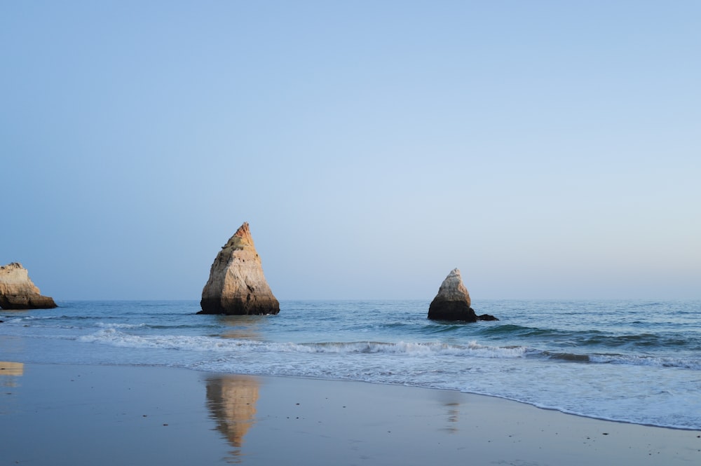 three rocks sticking out of the water on a beach