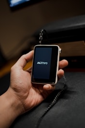 A hand is holding a small, portable electronic device with a screen displaying the word 'ACTIVO'. The device is connected to a black cable.