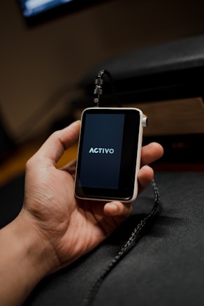 A hand is holding a small, portable electronic device with a screen displaying the word 'ACTIVO'. The device is connected to a black cable.