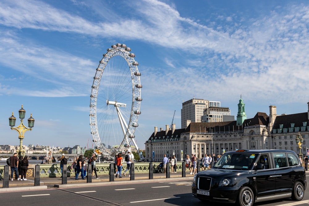 Ein schwarzes Auto, das neben einem Riesenrad eine Straße entlang fährt