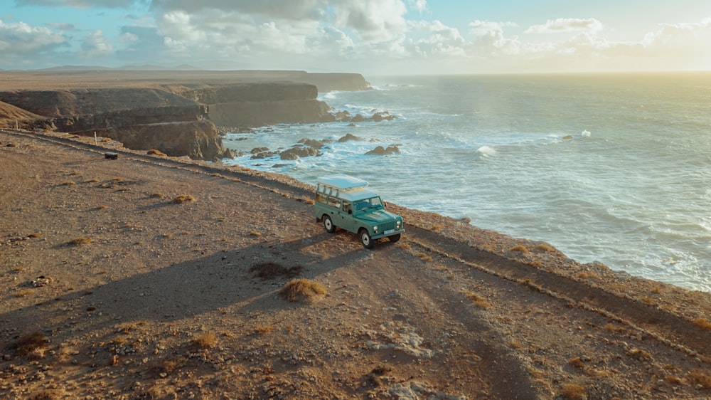 a jeep driving down a dirt road next to the ocean