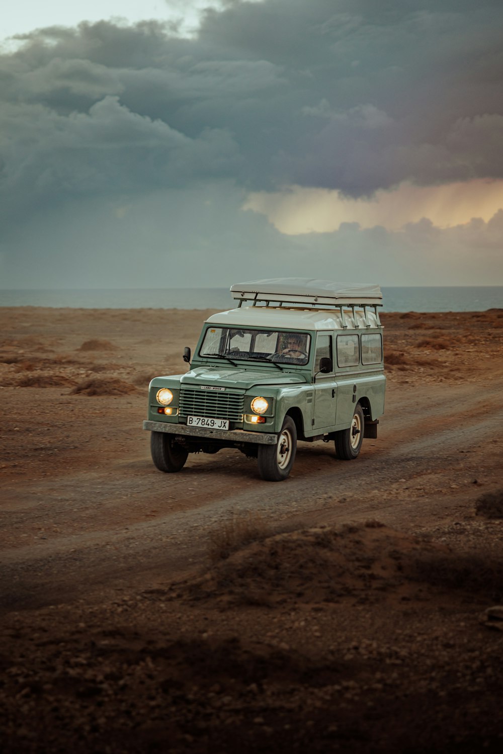 a green vehicle driving down a dirt road