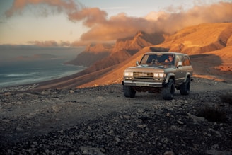A rugged 4x4 jeep climbing a misty mountain trail at dawn with glowing sunrise in the background.
