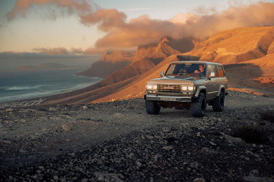 A 4WD vehicle towing a caravan through a scenic off-road trail at sunset.