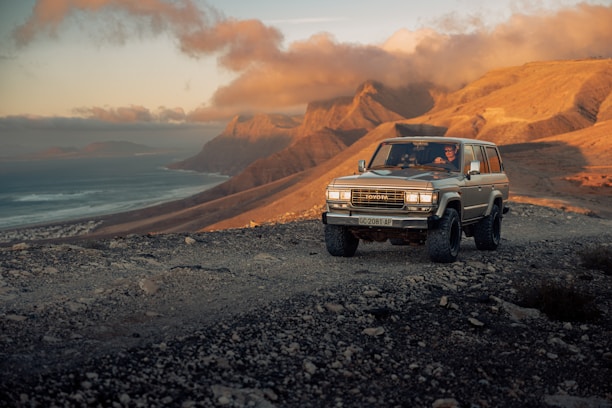 A rugged 4x4 jeep climbing a misty mountain trail at dawn with glowing sunrise in the background.