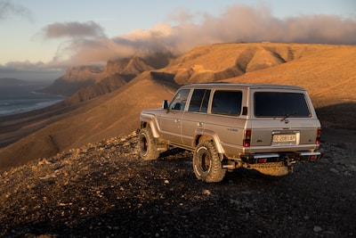 Panoramic view of the Atlas Mountains with a luxury 4x4 vehicle parked nearby.