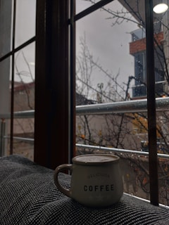 A cozy scene with a hand holding a warm ceramic coffee mug beside a window on a rainy day.