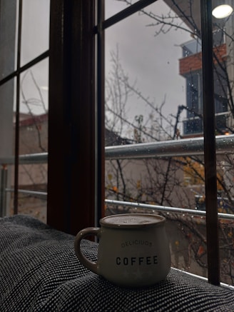 A cozy scene with a hand holding a softly textured ceramic mug beside a window with morning light.