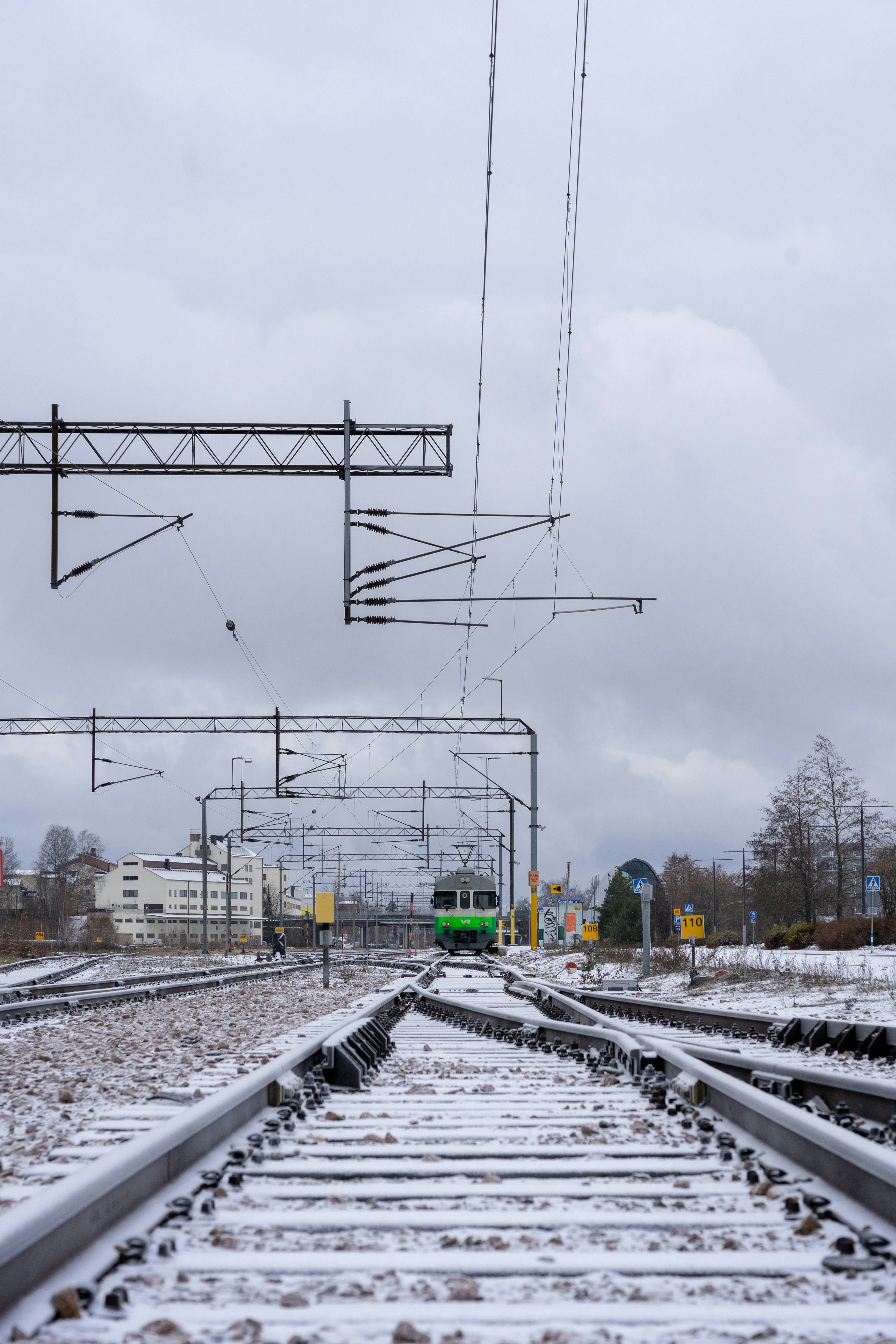 a green train traveling down train tracks under a cloudy sky