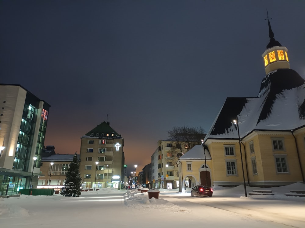 a snowy street with buildings and a clock tower in the background