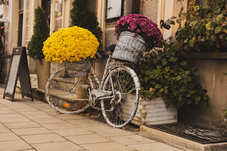 A colorful commuter bike with a basket full of fresh flowers parked outside a café