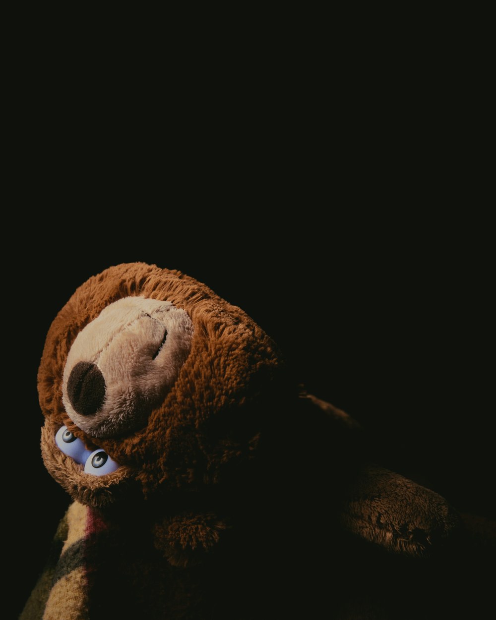 a brown teddy bear with blue eyes laying down