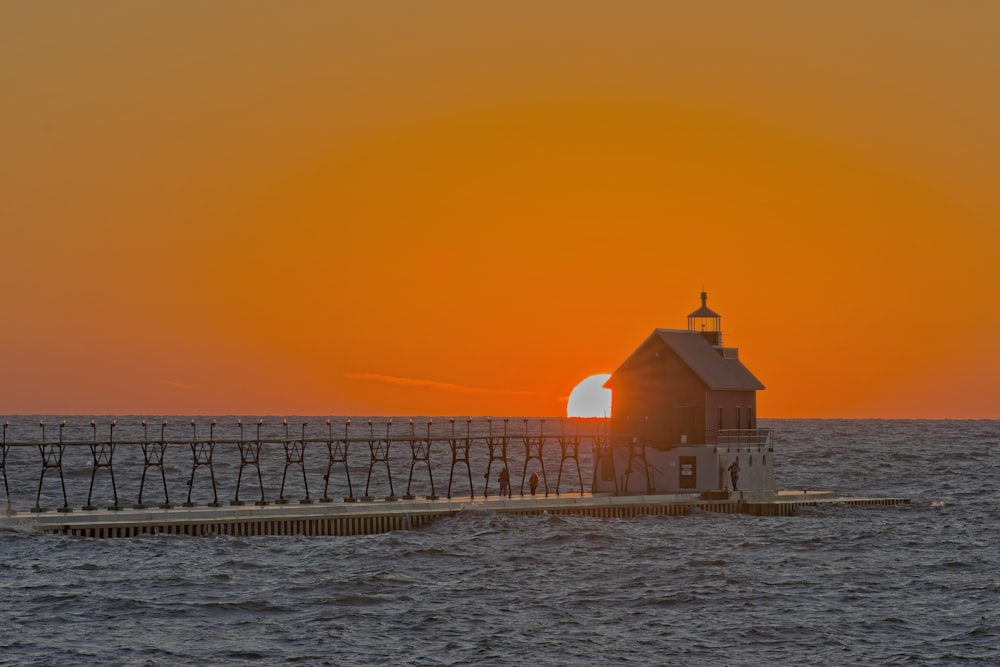 the sun is setting over the ocean with a lighthouse in the foreground