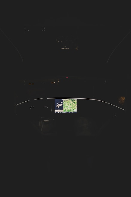 A dimly lit cockpit with a central screen displaying a map and an image of an aircraft, surrounded by other unlit controls and displays.