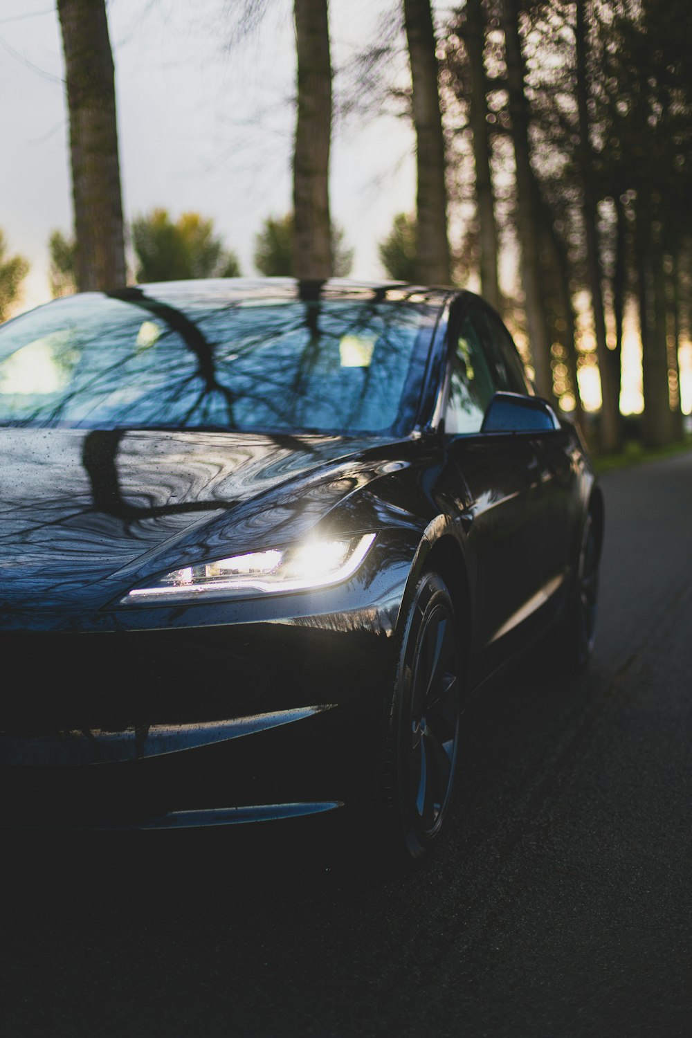 a black car driving down a street next to trees