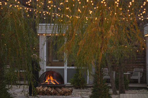 A cozy backyard scene featuring a glowing Lumea fire pit surrounded by friends sharing stories under string lights.