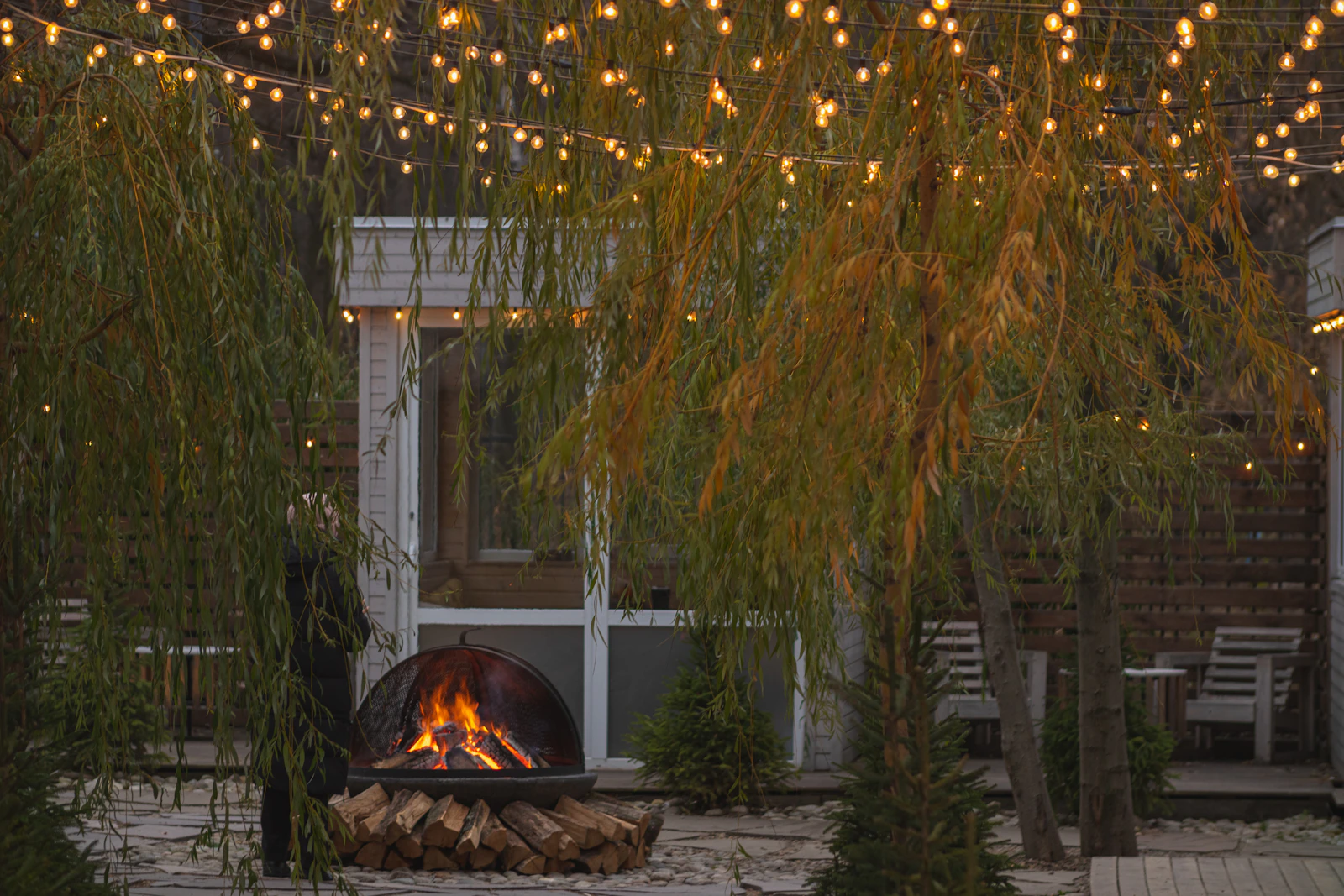 Premium paver patio with fire pit surrounded by trees and warm string lights at dusk