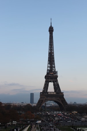 The Eiffel Tower is prominently featured against a clear blue sky. A bustling city landscape surrounds the tower, with many tourists and vehicles visible in the foreground, creating a lively atmosphere.