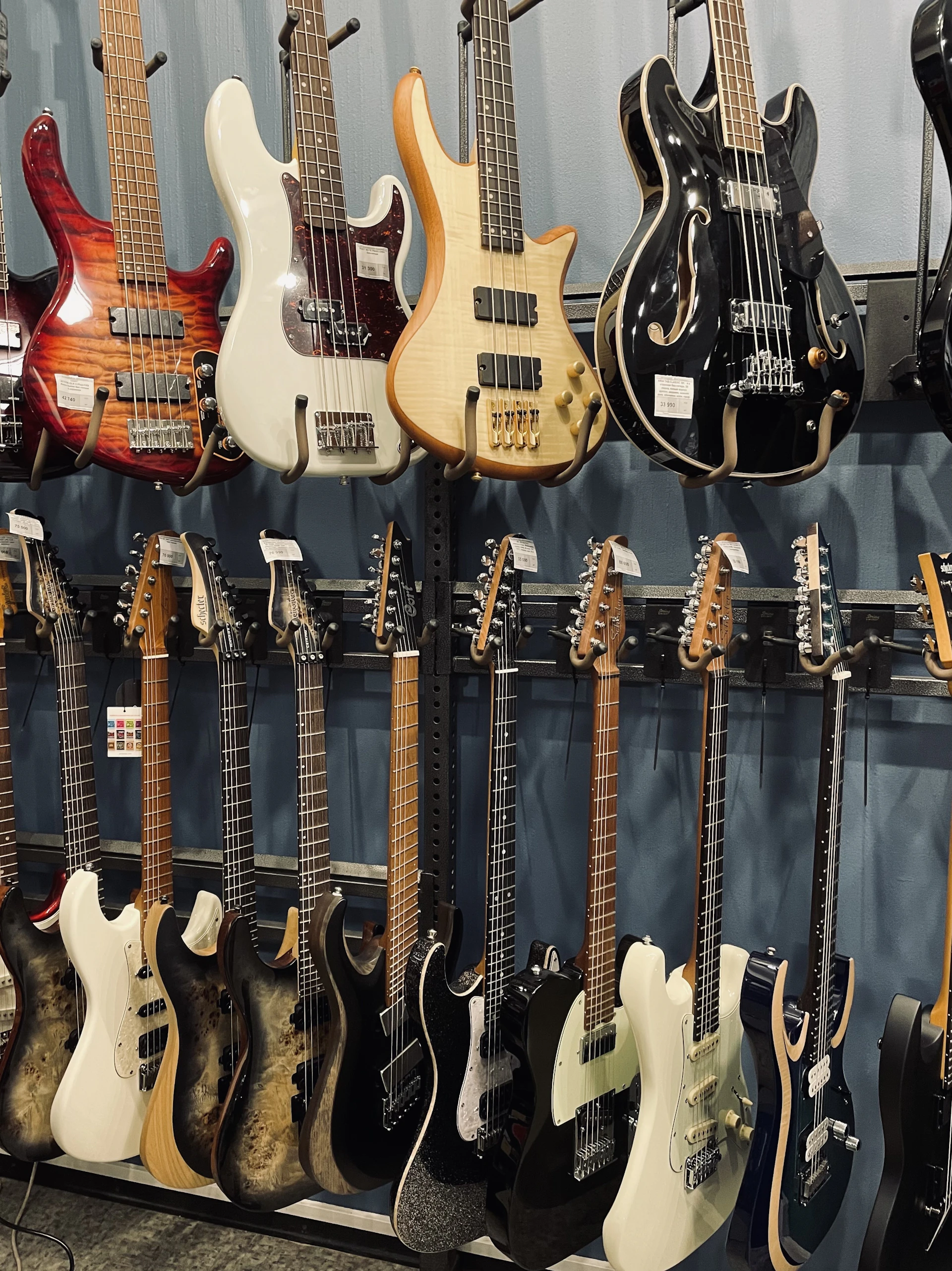 A lineup of bass guitars in various colors hanging on a display rack under warm lighting.