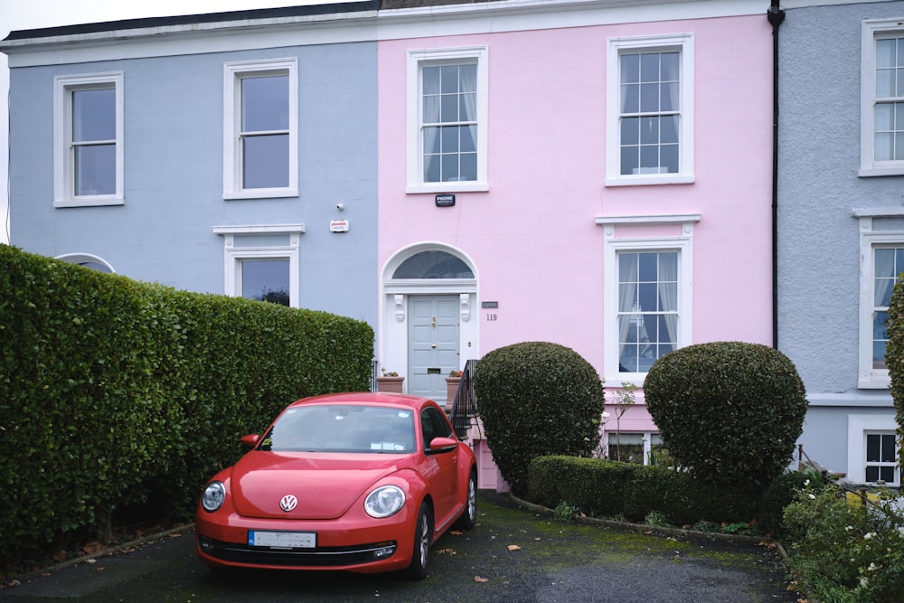 a red car parked in front of a pink house