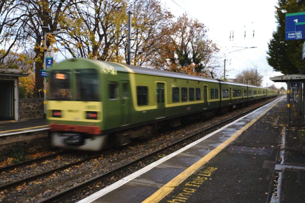 a green train traveling past a train station