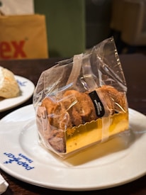 A plate with the logo 'Pepper') Thailand' holds a package of cookies wrapped in clear plastic with a gold-colored base. The cookies appear to be tied with a ribbon and have a small, black label attached.