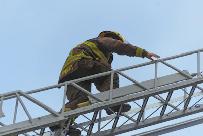 Firefighter climbing a ladder against a bright blue sky.