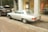 A vintage silver Mercedes-Benz car is parked on a cobblestone street beside a black Range Rover. The vehicles are near an art gallery with large glass windows displaying artwork and sculptures. Autumn leaves are scattered on the ground, adding a rustic touch to the urban setting.