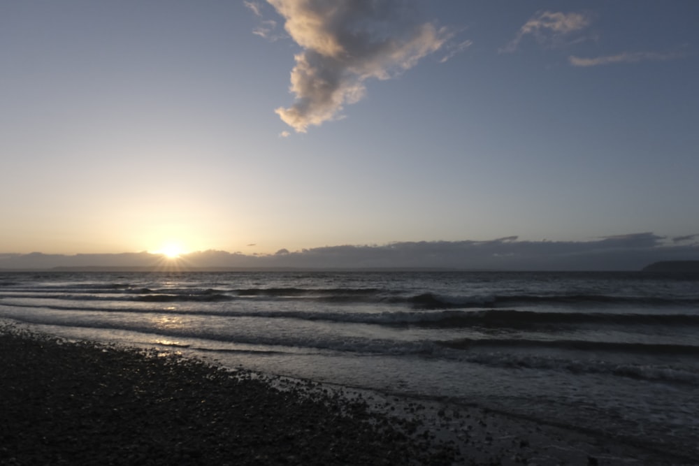 the sun is setting over the ocean with a cloud in the sky