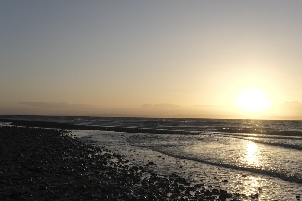 the sun is setting over the water at the beach