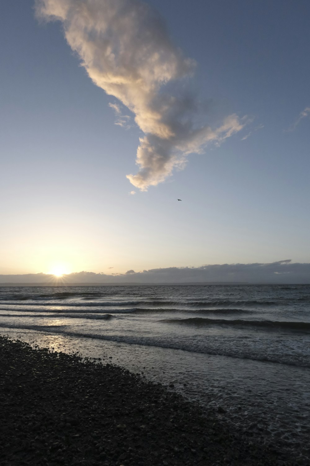 the sun is setting over the ocean with a cloud in the sky