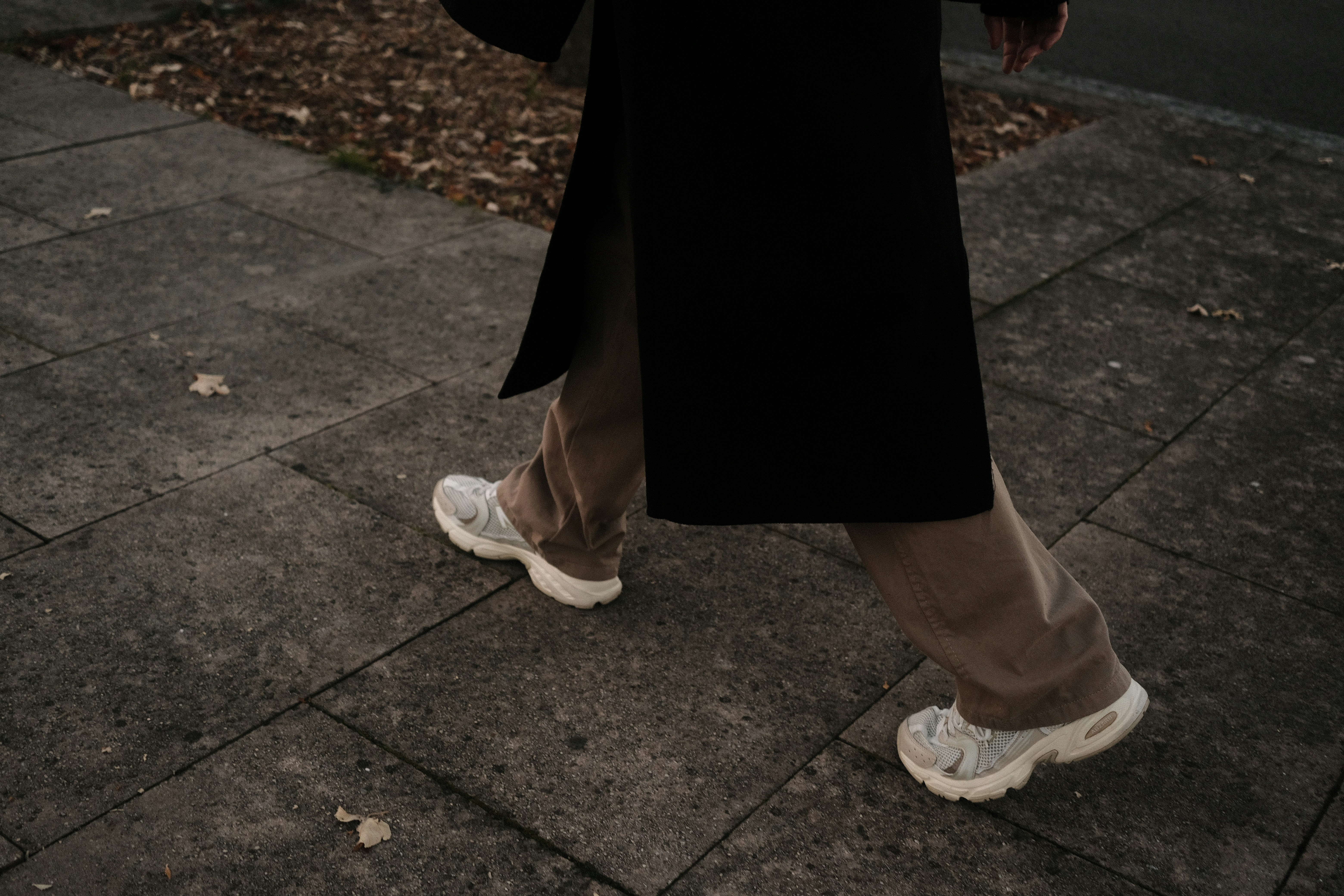 a person walking down a sidewalk in a black coat