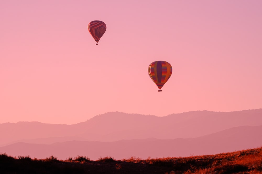 a couple of hot air balloons flying through a pink sky