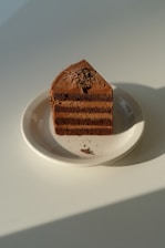 A close-up photo of a chocolate cake slice with creamy layers and chocolate shavings on top.