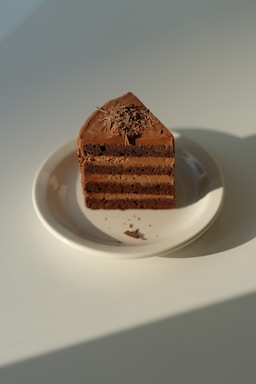 A close-up photo of a chocolate cake slice with creamy layers and chocolate shavings on top.