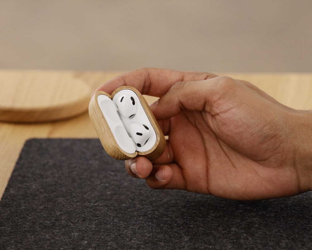 a person holding a wooden case with two airpods in it
