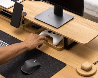 A cozy workspace with a laptop, smartphone, gaming controller, and movie tickets scattered on a wooden desk.