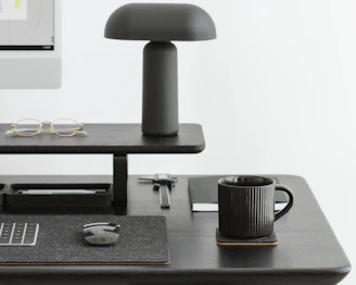 A sleek minimalist desk setup with a laptop, notepad, and a cup of coffee, all in black and beige tones.