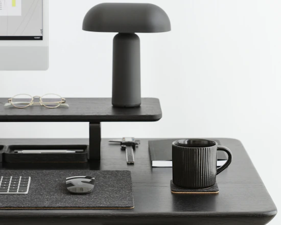 A sleek minimalist desk setup with a laptop, notepad, and a cup of coffee, all in black and beige tones.