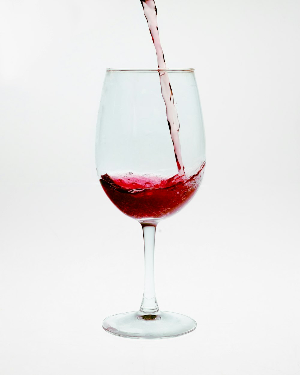 a wine glass filled with red wine being poured into it