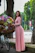 A cheerful woman standing beside a beautifully arranged flower stand at an outdoor event.