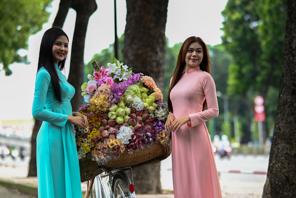 two women standing next to each other holding a basket of flowers