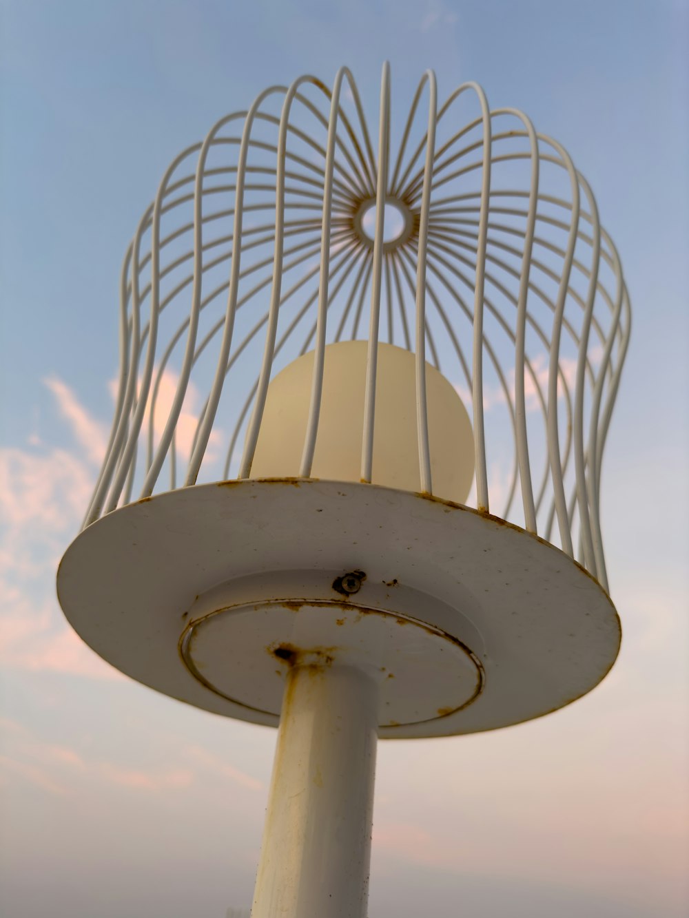 a white bird cage sitting on top of a metal pole