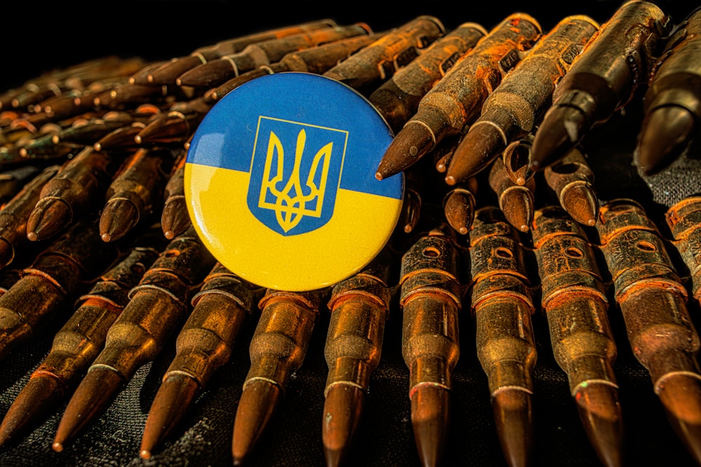 a blue and yellow button sitting on top of a pile of bullet shells