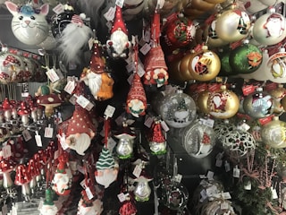 A collection of Christmas ornaments featuring gnome figures, mushrooms, and various festive baubles with intricate designs. There are ornaments with red hats, white beards, and whimsical expressions. The baubles include gold, green, and red colors with depictions of Santa and other holiday motifs.