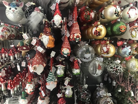 A collection of Christmas ornaments featuring gnome figures, mushrooms, and various festive baubles with intricate designs. There are ornaments with red hats, white beards, and whimsical expressions. The baubles include gold, green, and red colors with depictions of Santa and other holiday motifs.