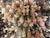 An assortment of decorative ballerina ornaments is displayed on hooks. The ballerinas are adorned with detailed tutus in various colors including pink, white, and gold, and some are embellished with glitter. Surrounding them are complementary decorative items like embroidered fabric and floral designs.