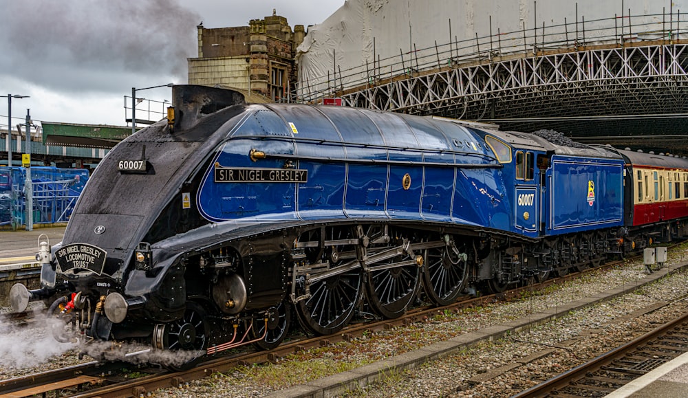 a blue train traveling down train tracks next to a bridge