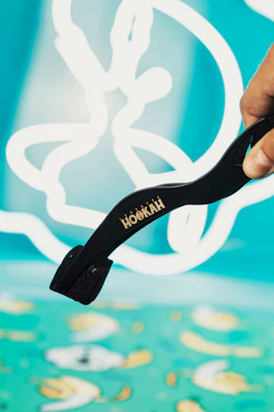 A hand holding a pair of tongs lifting a hot coal above a modern hookah bowl.